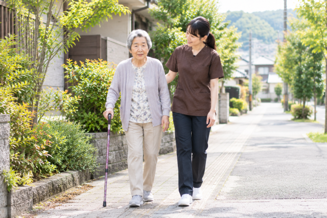 脳卒中後の女性が理学療法士と屋外で歩行練習をしている様子
